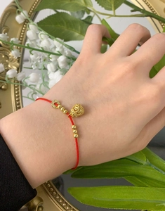 Detailed view of red woven money bag bracelet with gold charms on female wrist