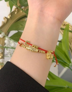 Close-up of red woven cord bracelets with golden charms on a female wrist