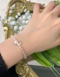 Détail du bracelet en perles de cristal transparent porté au poignet sur fond fleuri