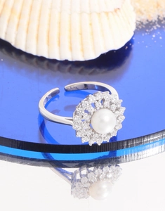 Macro detail of S925 silver pearl ring with sparkling zircon halo on blue reflective stand