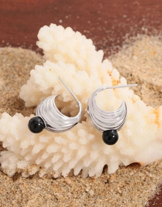 Detail of silver crescent earrings with wavy texture and black onyx beads on white coral