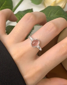 Close-up of S925 silver ring with oval strawberry crystal on model's hand with flowers