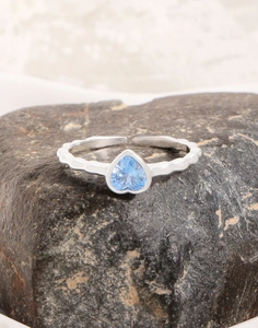 Detail of S925 sterling silver ring with blue heart zircon on natural rock surface