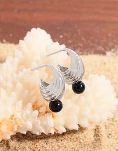 Macro shot of silver S-shape wavy earrings with black onyx beads on coral stone