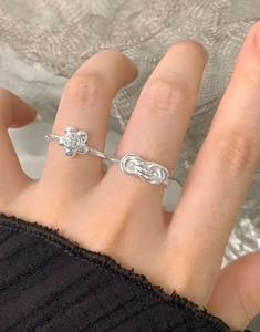 Detail showing a silver floral zircon ring and infinity knot ring on a finger