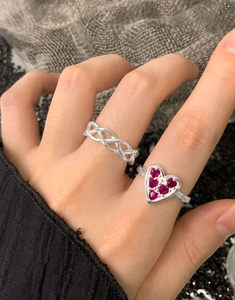 Detail of S925 silver heart ring with red zircons and twisted braided band on finger