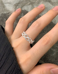 Detailed view of silver braided crossover ring worn on finger featuring mesh texture