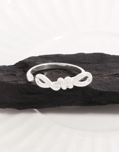Close-up of polished S925 sterling silver bow knot ring on textured black coal