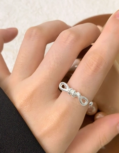 Macro shot of minimalist silver bow ring showing refined metallic luster on hand