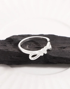 Macro shot of silver bow ring on charcoal texture emphasizing high gloss finish