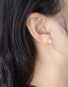 Close-up of model wearing small hollow flower stud earrings with white pearl center