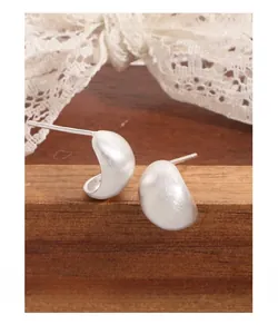 Gros plan de boucles d'oreilles argentées mates en forme d'œuf sur bloc de bois
