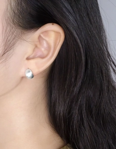 Détail macro de boucles d'oreilles minimalistes en argent mat sur l'oreille du modèle