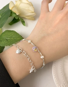Detailed close-up of double-layer silver bracelets featuring starfish, shells, and pearls