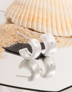 Macro shot of silver C-shaped brushed star stud earrings on a reflective mirror surface