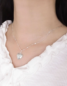 Close-up of S925 sterling silver heart pendant with bow relief on delicate bead chain