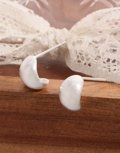 Détail macro de boucles d'oreilles argentées mates avec poinçon S925 sur un plateau en bois
