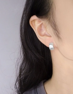 Macro detail of brushed silver starburst stud earrings featuring matte finish on model