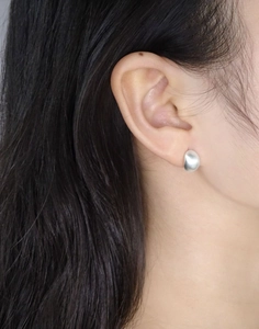 Détail de boucles d'oreilles minimalistes en argent mat en forme d'œuf sur le lobe