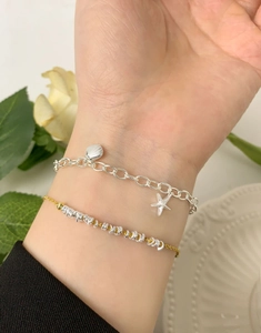 Close-up of layered silver starfish and seashell charms on bracelets with floral decor