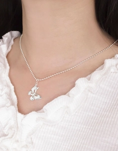Close-up of a silver butterfly pendant on a beaded chain worn by a model in lace