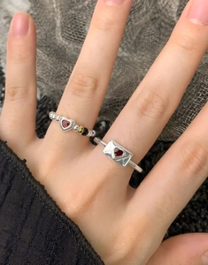 Dettaglio dell'anello a busta in argento S925 e fascia con perline cuore rosso sul dito