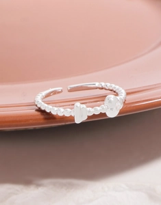 Macro shot of silver beaded adjustable ring with irregular geometric charms on ceramic