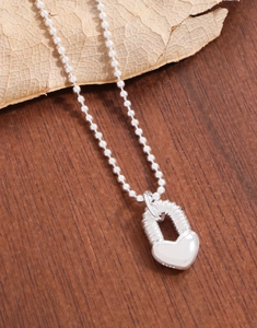 Gros plan du pendentif cadenas cœur en argent S925 avec poinçon sur socle en bois