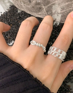 Detail of S925 sterling silver hollow chain and bow rings set on black sand texture