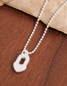 Vue macro d'un pendentif cadenas en forme de cœur argenté avec chaîne à billes sur bois