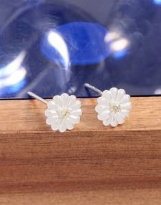 Macro detail of silver daisy earrings with yellow gemstone on a wood display stand