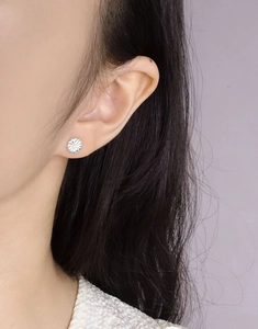 Daisy shaped silver stud earrings with yellow center shown worn on a model's ear