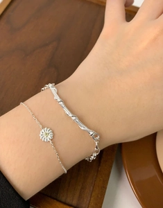 Detailed view of stacked S925 silver daisy flower charm bracelet and rope chain on wrist