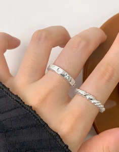 Detailed view of silver twist ring and heart engraved band worn together on model
