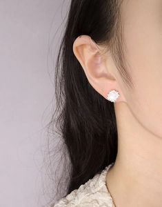 Macro shot of a floral silver earring with a round white gem worn by a model