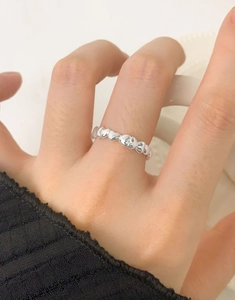 Close-up of minimalist heart-shaped silver ring on finger with white background