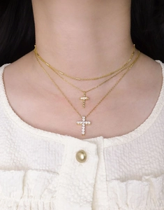 Détail de colliers superposés en or avec pendentifs croix et zircons brillants