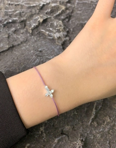 Macro detail of a purple cord bracelet with a sparkling zircon cross pendant