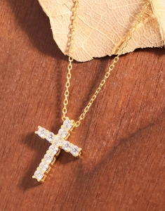 Détail du collier croix en argent doré orné de zircons blancs sur fond en bois