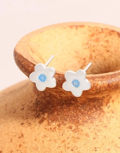 Makroaufnahme von S925 Silber Blumenohrsteckern mit blauem Zirkon auf einem Keramikglas