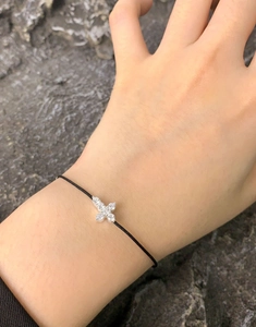 Macro detail of zircon cross bracelet with black woven cord on hand over grey stone