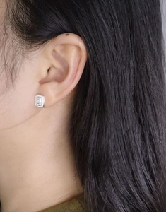 Detail of square silver stud earring with textured metal surface worn by a model