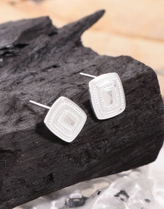 Macro detail of silver geometric square stud earrings with zircon on black charcoal stone