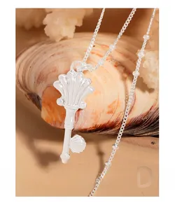 Macro shot of silver key necklace with shell pendant on beach sand and coral decor