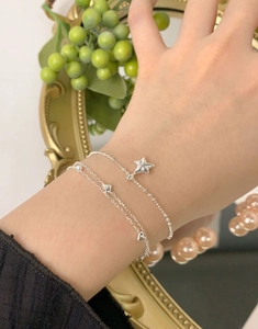 Dettaglio dei bracciali a strati in argento S925 con stella e cuore sul polso di una donna