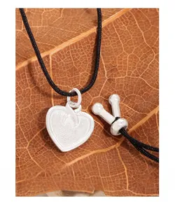 Macro shot of S925 sterling silver heart pendant on black cord over autumn leaves