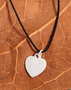 Detailed close-up of S925 sterling silver heart pendant on black cord over leaf
