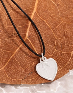 Macro shot of silver heart pendant with black cord on a textured autumn leaf background