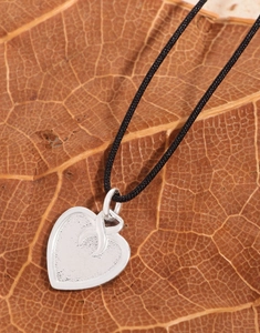 Macro shot of silver heart pendant with black cord on a textured dry leaf background