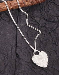 Detailed view of an engraved silver heart pendant necklace on a natural wood background